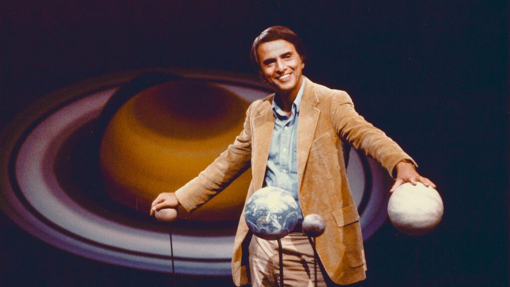 Carl Sagan standing in a model of the solar system.